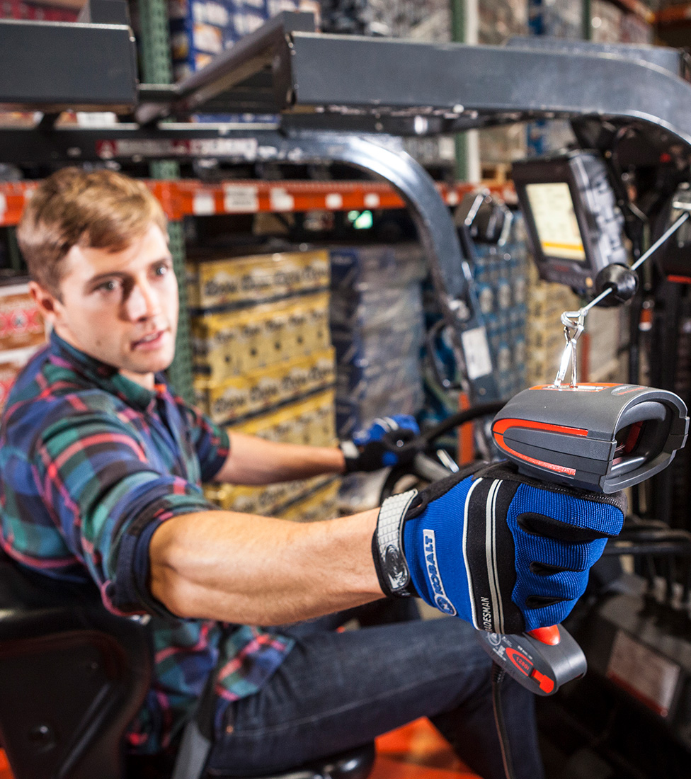 A warehouse employee using a handheld scanner while using a forklift.